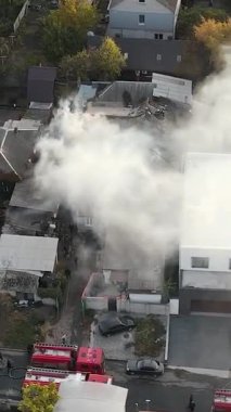 Bir yerleşim bölgesinde büyük bir yangınla mücadele: özel bir evin kömürleşmiş çatısında çalışan itfaiyecilerin havadan görünüşü, mahallenin üzerine yoğun duman yükseliyor. Kurtarma ekipleri ve itfaiye araçları olay yerinde..