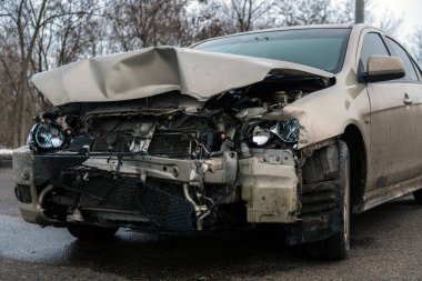 Kötü deforme olmuş bir kaput, kırık farlar ve yolda hasarlı bir radyatör ile kaza yaptıktan sonra kaza yapmış bir arabanın ön tarafında..