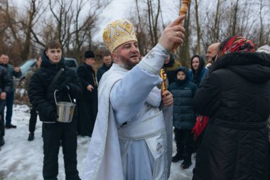 Bir Ortodoks rahibi kutsal su ayinini gerçekleştirir. Rahip kör edici bir madde kullanarak kutsal su serpiyor. Kışın geleneksel bir dini tören. Belgesel fotoğrafçılık. Suyun vaftiz töreni..