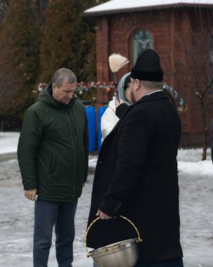 Bir Ortodoks rahibi kutsal su ayinini gerçekleştirir. Rahip kör edici bir madde kullanarak kutsal su serpiyor. Kışın geleneksel bir dini tören. Belgesel fotoğrafçılık. Suyun vaftiz töreni..