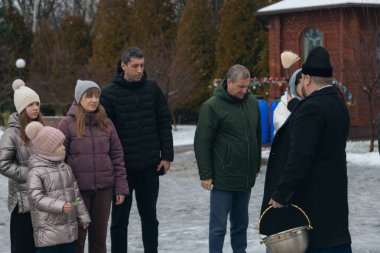 Bir Ortodoks rahibi kutsal su ayinini gerçekleştirir. Rahip kör edici bir madde kullanarak kutsal su serpiyor. Kışın geleneksel bir dini tören. Belgesel fotoğrafçılık. Suyun vaftiz töreni..