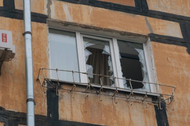Bombardımandan sonra çok katlı bir binanın kırık penceresinin yakın çekimi. Çerçevede keskin cam parçaları ve boş pencere açıkları hasarlı binanın pervazının arka planına karşı görünür..