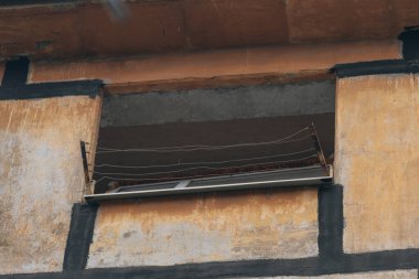 Yıkılmış bir konut binasında boş bir pencerenin açılışı. Kayıp çerçeve ve hayatta kalan çamaşır ipleri, doğrudan ya da güçlü bir patlama sonrasında periye verilen hasarın boyutunu vurguluyor..