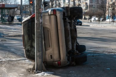 Şehir caddesinde geçirdiği bir kazadan sonra altın rengi bir SUV 'nin dikiz aynasından devrildi. Araç elektrik direğine dayanıyor. Şasi ve vücut hasarını gün ışığında gösteriyor.