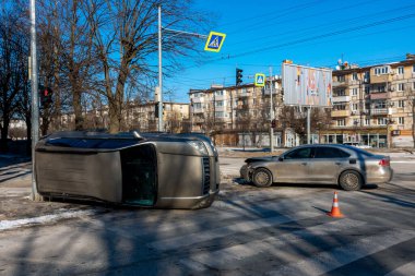 Şehir kavşağında çok araçlı bir kazanın geniş açılı görüntüsü. Yan tarafında bir trafik lambasının yanında duran altın rengi bir SUV, ön tarafında hasar olan gümüş bir sedan ise asfaltta duruyor.