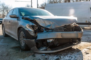 Çarpışmadan sonra ön yüzünde geniş çaplı hasar olan gümüş renkli bir sedan. Görüntü buruşmuş bir başlık, kırılmış farlar ve şehir sokaklarının birinde ayrılmış bir tampon gösteriyor.