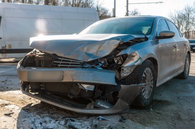 Çarpışmadan sonra ön yüzünde geniş çaplı hasar olan gümüş renkli bir sedan. Görüntü buruşmuş bir başlık, kırılmış farlar ve şehir sokaklarının birinde ayrılmış bir tampon gösteriyor.