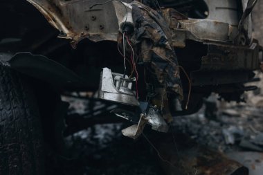 Açığa çıkmış kabloların yakın çekimi ve parçalanmış bir araçtan sarkan kırık bir far. Patlamadan ya da bombardımandan sonra sivil bir aracın enkazı. Kentsel savaş sonrası ve altyapı kaybı kavramı.