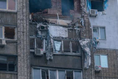 Patlama ya da füze saldırısından sonra bina cephesinde yıkılmış. Kırık camlar, hasarlı tuğla duvarlar ve bir apartmanın enkazı. Savaş sonuçları, felaket sonrası, mülkiyet tahribatı ve insani yardım krizi kavramı.