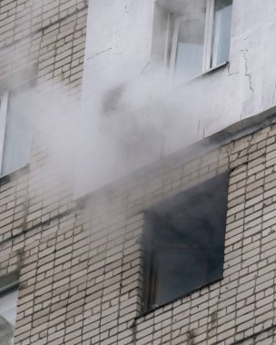 Kırık bir penceresi ve yoğun dumanı olan tuğlalı bir binanın ön cephesine yakın çekim. Çok katlı bir binada çıkan yangın ya da bombardıman sonrası şehrin yıkımı ve acil durumu belgeleniyor..