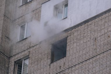 Kırık bir penceresi ve yoğun dumanı olan tuğlalı bir binanın ön cephesine yakın çekim. Çok katlı bir binada çıkan yangın ya da bombardıman sonrası şehrin yıkımı ve acil durumu belgeleniyor..