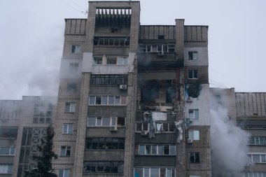Bir top mermisi ya da patlamayla vurulduktan sonra çok katlı Doğu Avrupa tarzı bir konut binasının genel görünümü. Birkaç kattaki yıkılmış daireler, kırık camlar, yangın izleri ve bulutlu bir kış gününde binadan yükselen duman..
