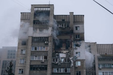 Bir top mermisi ya da patlamayla vurulduktan sonra çok katlı Doğu Avrupa tarzı bir konut binasının genel görünümü. Birkaç kattaki yıkılmış daireler, kırık camlar, yangın izleri ve bulutlu bir kış gününde binadan yükselen duman..