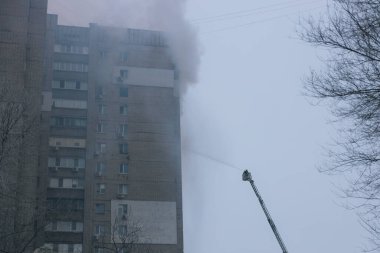 İtfaiyeciler kışın acil kurtarma operasyonu sırasında dumanla dolu bir konut binasının üst katlarına ulaşmak için iki uzun hava merdiveni kullanırlar.