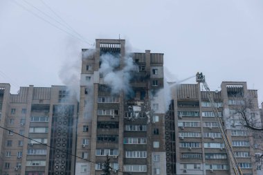 Yükseltilmiş bir Magirus döner merdivenindeki itfaiyeciler yüksek basınçlı bir hortumla patlama veya yangın sonucu hasar görmüş çok katlı bir binaya su sıkarlar. Birkaç yıkılmış balkondan yükselen duman ve kırılmış camlar görülüyor.