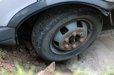 Çukurun kenarındaki yumuşak toprağa sıkışmış bir araba lastiğinin yakın çekimi. Çamurdaki lastik ve hasarlı zeminin ayrıntıları. Şehirde yaşanan acil bir durumu belgeleyen bir haber raporu..
