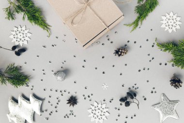 Pastel arka planda ardıç dalları, çam kozalakları, dekoratif köknar ağacı, toplar, gümüş kar taneleri, yıldızlar ve pullarla dolu el işi bir kutu. Noel hediyesi. Kutlama ve parti konsepti. Düz yatıyordu. Üst görünüm