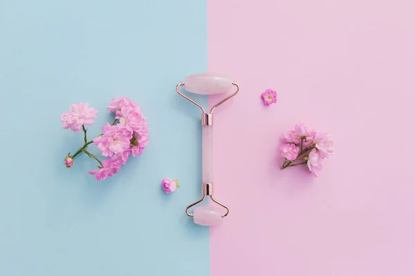 Ev spası için yüz masajı seti. Gül tomurcuklarıyla pembe ve mavi pastel arka planda gül kuvarsından yapılmış yüz silindiri ve gua sha masaj aleti. Doğal tedavi kavramı.