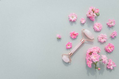 Ev spası için yüz masajı seti. Gül tomurcuklu pastel arka planda gül kuvarstan yapılmış yüz silindiri ve gua sha masaj aleti. Doğal tedavi kavramı.