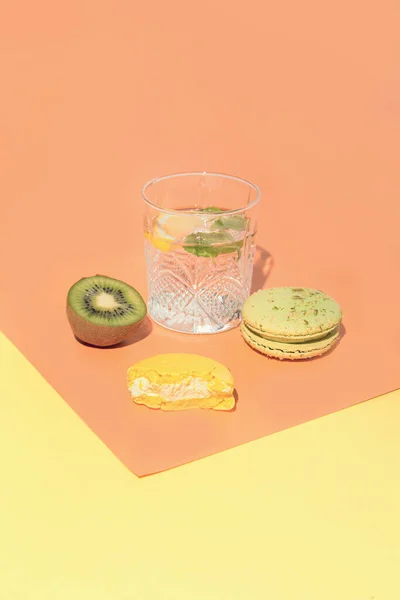 Bite macaroon, glass of lemonade and half of kiwi fruit on colorful geometric background. Minimal style composition