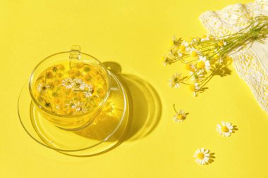 Sarı arka planda bir fincan papatya çayından yapılmış yaratıcı bir kompozisyon. Rahatlamak için doğal bitkisel içecek. Doğa konsepti.