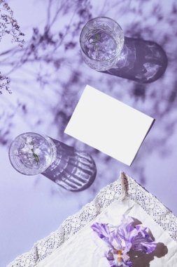 İki bardak su ve üzerinde süsen çiçeği olan iki bardak beyaz bez ve gölgeli eflatun arkaplan. Yaz tatili konsepti. Düz güneş ışığı yatıyordu. Asgari düzeyde. Üst görünüm