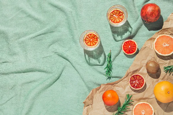 Meyve, biberiye, bir bardak su ve pastel yeşil plaj havlusu üzerine kitaplar. İçkiler ve içecek konsepti. Düz güneş ışığı yatıyordu. Asgari düzeyde. Üst görünüm.