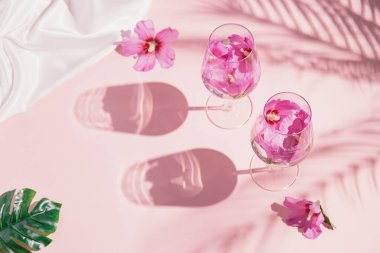 İki bardaktan oluşan yaratıcı kombinasyon. İçinde çiçek suyu ve pastel pembe arka planda palmiye yaprakları gölgeleri ve canavar yaprağı var. Yaz ve ferahlatıcı konsept