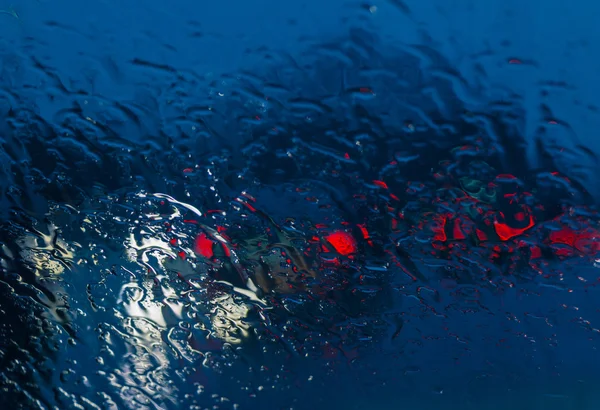Camino de la ciudad visto a través de gotas de lluvia en el parabrisas del coche — Foto de Stock