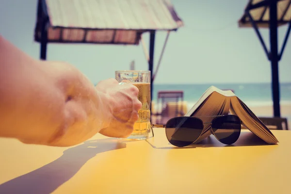 Του ανθρώπου χέρι που κρατά ένα ποτήρι μπίρα σε ένα καφέ παραλία. Διακοπές το — Φωτογραφία Αρχείου