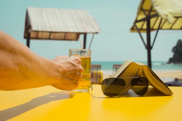 Bir bardak bira bir plaj kafede tutan elini. Tatil