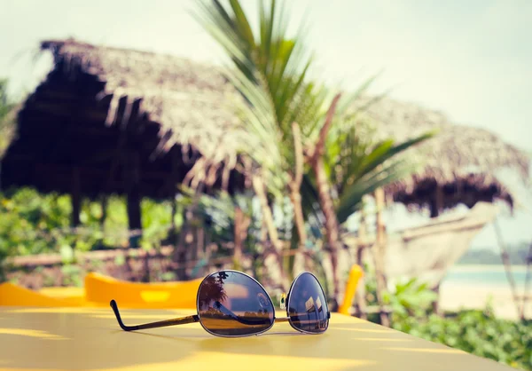 Óculos de sol deitados em uma mesa amarela em um café tropical de praia — Fotografia de Stock