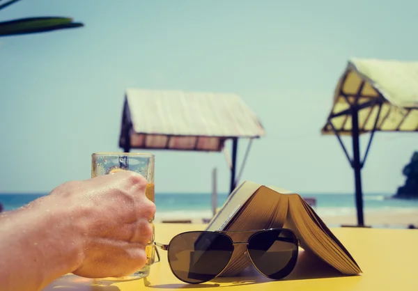 A mão de um homem a segurar um copo de cerveja num café de praia. Férias o — Fotografia de Stock