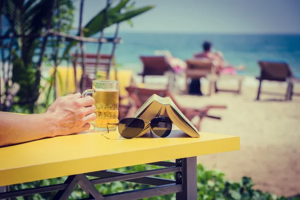Man's hand holding a glass of beer in a beach cafe