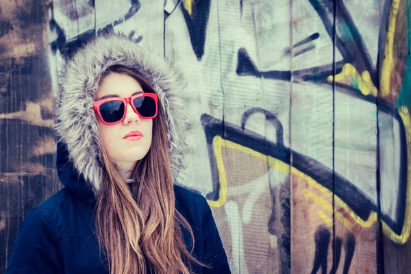 Portrait of a teenage girl wearing red sunglasses and coat hood — Stock Photo, Image