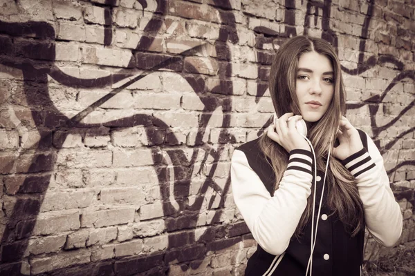 Teenage girl  with headphones near fragment of a graffiti wall — Stock Photo, Image