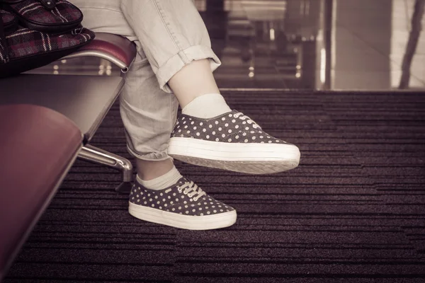 Una chica sentada en una silla. Vista de pies en zapatillas y jeans — Foto de Stock