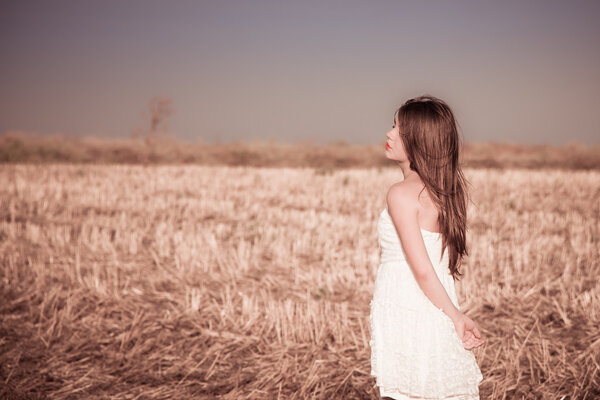 A girl with long hair in a white dress posing in a summer field