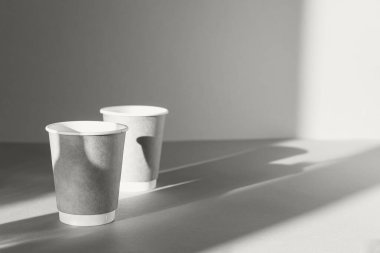 Güneşli arka planda gölgeli iki kağıt bardaktan oluşan yaratıcı kompozisyon. Asgari düzeyde. Sabah içkileri ve içecek konsepti. 2026 yılının rengi