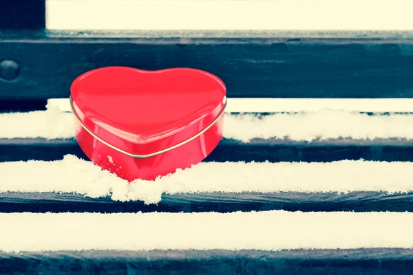 Scatola di latta a forma di cuore rosso su una panchina coperta di neve — Foto Stock