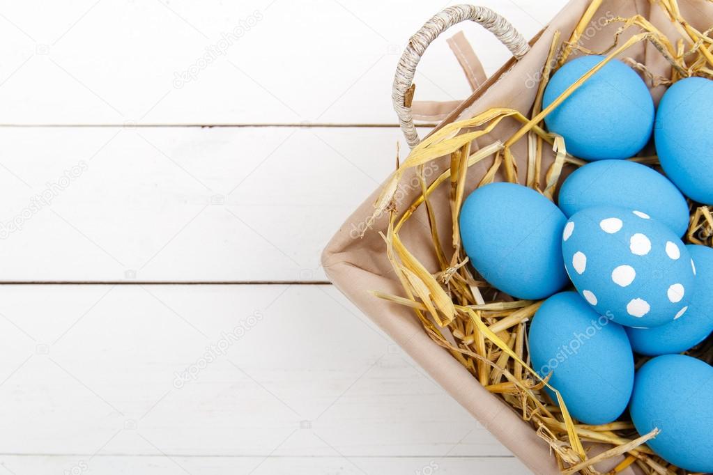 Blue easter eggs in a basket on a white wooden table