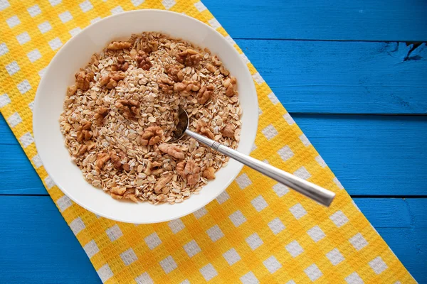 Mavi ahşap bir masa peçete dekor beyaz bir tabağa ceviz ile kuru yulaf gevreği. Fındık yulaf ezmesi. Üstten Görünüm noktası.