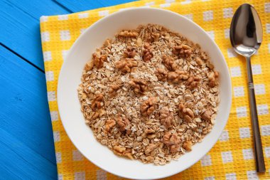 Mavi ahşap bir masa peçete dekor beyaz bir tabağa ceviz ile kuru yulaf gevreği. Fındık yulaf ezmesi. Üstten Görünüm noktası.