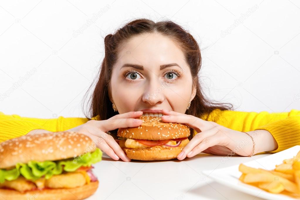 Girl bites off a huge hamburger. Unhealthy diets. 