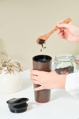 Kadın, kahverengi termosu olan bardakta çay demliyor. Cam bir kavanozun arka planında tatlı bir tahta kaşık tutuyor. Yanında da bol çay var. Sağlıklı gıda konsepti. 