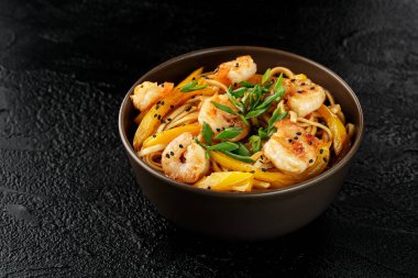 Karidesli yumurta eriştesi, sarı biber ve siyah arka planda koyu kahverengi bir tabakta susam tohumları. Asya yemekleri.