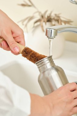 Kadın, metal bir şişeyi hindistan cevizi fırçasıyla yıkıyor. Bulaşıkları kimyasalsız yıkamak. Kadın, metal bir şişeyi hindistan cevizi fırçasıyla yıkıyor. Bulaşıkları kimyasalsız yıkamak. 