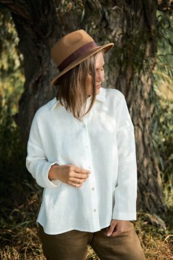 Beyaz keten gömlekli ve şapkalı güzel kız dinleniyor ve yaz gününün tadını çıkarıyor ve parkta yürüyor..