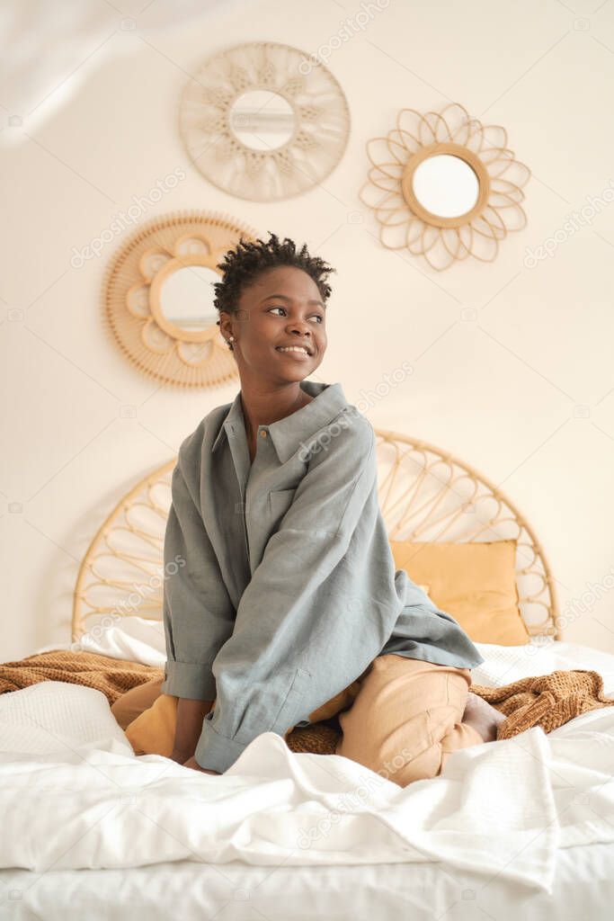 Young girl in a beautiful loose linen shirt is having fun on the bed. Smiles and looks away.