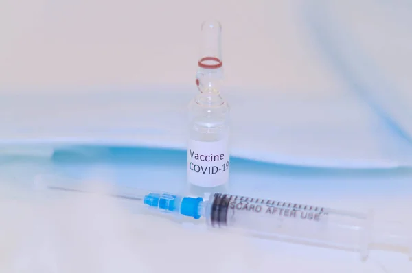 A vial bottle of coronavirus vaccine along with injection syringe, on white studio and mask background.